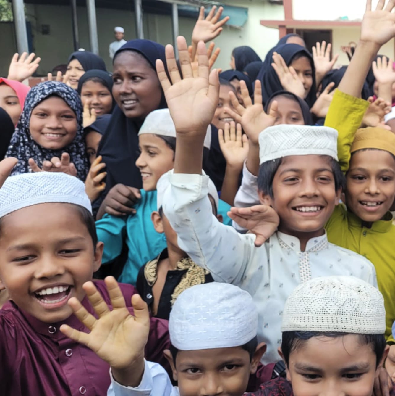 Groupe d'enfants souriants levant la main, rassemblés à l’extérieur pour une photo de groupe joyeuse.