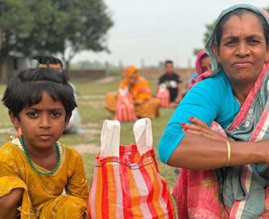 Une femme et une fillette assises à l’extérieur avec des sacs de dons alimentaires — action humanitaire de l’association Les P’tits Villages d’Afrique
