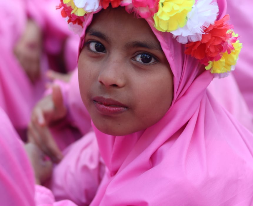 Jeune fille souriante vêtue d’un voile rose et d’une couronne de fleurs colorées, regardant l’objectif