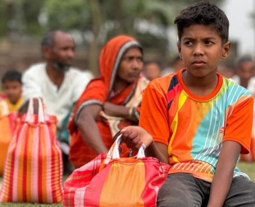 Jeune garçon tenant un sac de vivres coloré, assis parmi d’autres personnes lors d’une distribution humanitaire