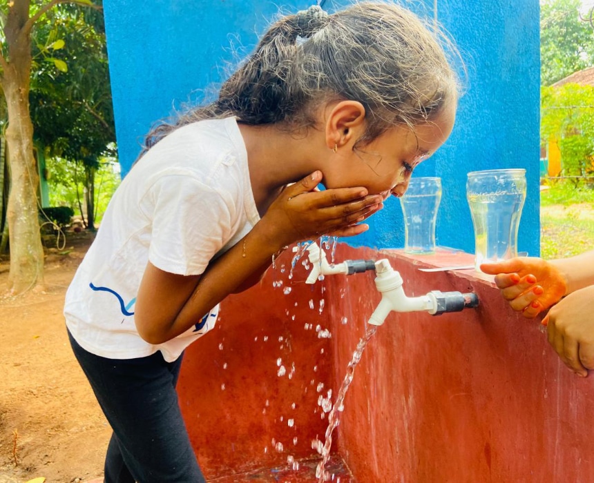 Jeune fille buvant et se rafraîchissant avec de l’eau propre à un point d’eau installé dans son village