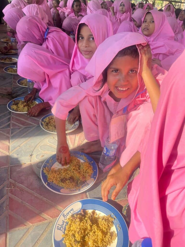 Offrir un repas : Jeunes orphelines au Bangladesh partageant un repas chaud offert par l’association Les P’tits Villages d’Afrique, souriantes et vêtues d’un uniforme rose.